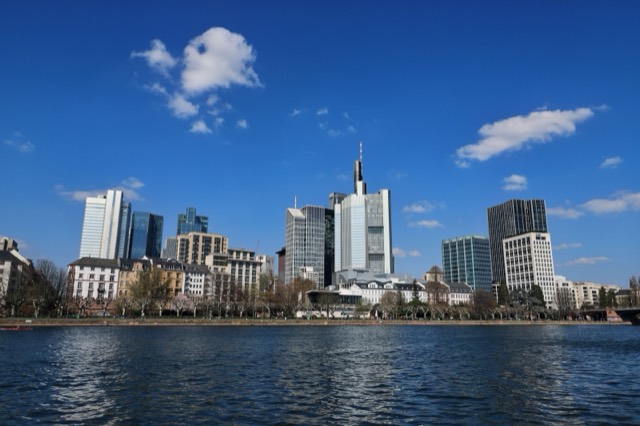 A stunning view of Frankfurt's skyscrapers reflecting on the River Main under a clear blue sky.